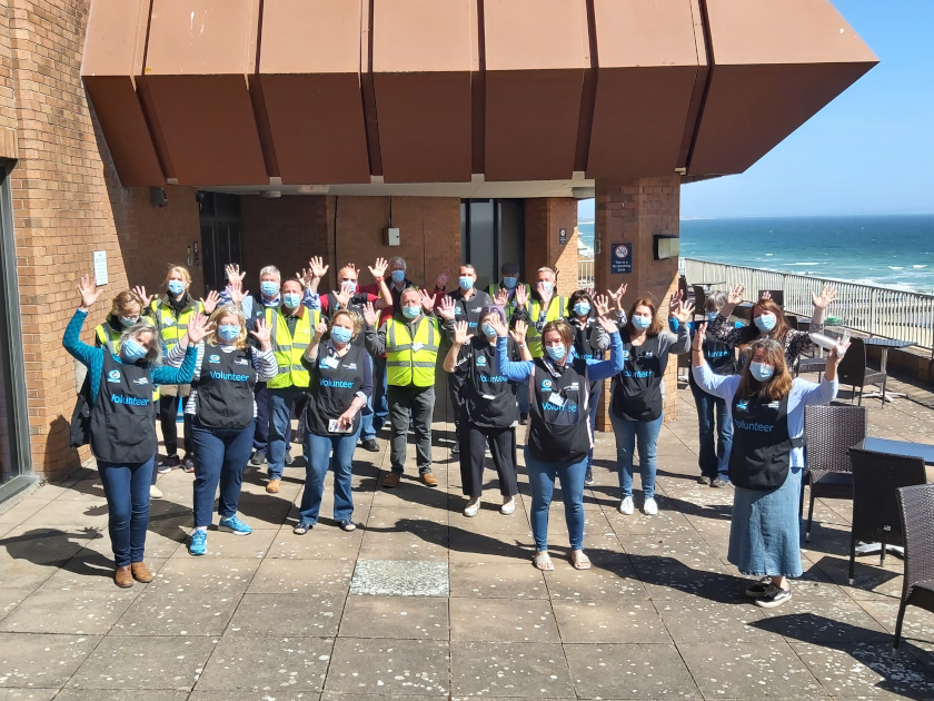 group of volunteers cheering in front of a building by the seaside 